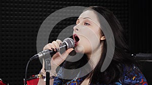 Emotional female vocal singing in microphone at recording studio. Singer is performing emotional lyric love song at rehearsal stud