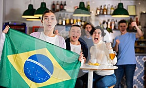 Emotional friends, football fans cheering for favorite Brazil team together while watching match on tv in bar