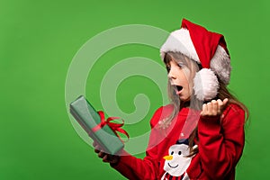 Emotional girl in a knitted sweater and Santa's hat looks in surprise at a cool gift. Guess the surprise. Merry