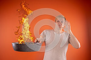 Emotional guy holding a frying pan in his hands, on an orange background.