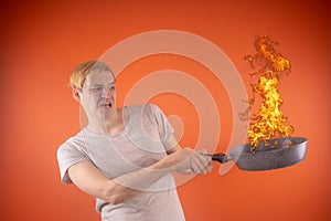 Emotional guy holding a frying pan in his hands, on an orange background.