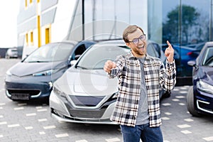 Emotional guy holding key in hand and smiling at camera. Man showing key from his new electric car. Young man buying auto at