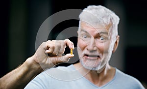 Emotional Handsome gray haired senior man with a pill in his hand. Medicine and health care concept