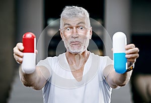 Emotional Handsome gray haired senior man with a pill in his hand. Medicine and health care concept