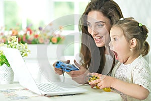 Emotional happy mother and daughter using laptop playing video game