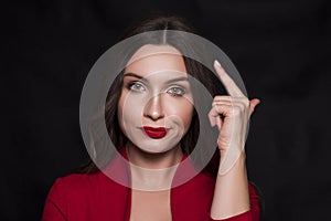Emotional head shot portrait of a brunette caucasian woman in red dress and with red lips on black background. She make disdain, photo