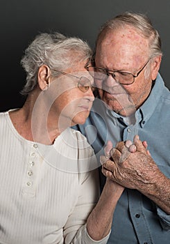 Emotional image of Senior couple holding hands in a tender loving embrace, both wearing glasses, man unshaven
