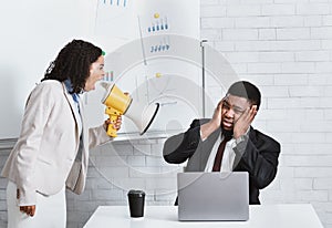 Emotional lady boss with megaphone screaming at male employee at workplace