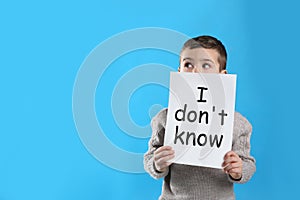 Emotional little boy holding paper with text I Don`t Know on light blue background photo