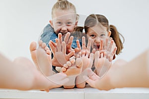 Emotional little siblings sitting with bare feet. Hands reaching them to tickle