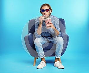 Emotional man with 3D glasses and popcorn sitting in armchair during cinema show