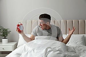 Emotional man with alarm in bed. Being late because of oversleeping