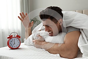 Emotional man with alarm in bed. Being late because of oversleeping