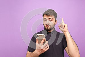 Emotional man with a beard holds a smartphone in his hands, showing his finger up in a blank space.Surprised adult in a dark shirt