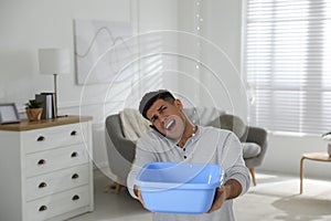 Emotional man calling roof repair service while collecting leaking water from ceiling in living room