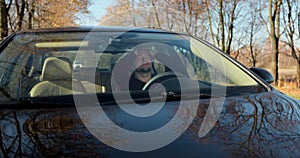 Emotional man in car, view through windshield. Aggressive driving behavior. Angry man driver hitting the steering wheel