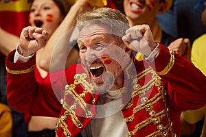 Emotional man, football, soccer fan expressively watching match, cheering up favourite team. Fans wearing colorful