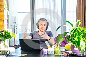 Emotional man in headphones looking at computer screen, gestures and participating in online meeting, conference with business par