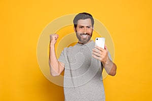 Emotional man looking at smartphone on yellow background