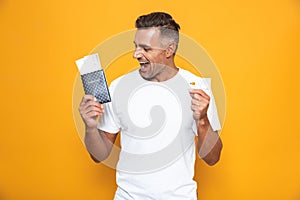 Emotional man posing isolated over yellow wall background holding passport with tickets