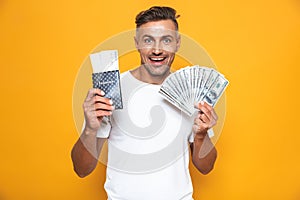 Emotional man posing isolated over yellow wall background holding passport with tickets and money