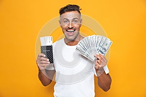 Emotional man posing isolated over yellow wall background holding passport with tickets and money