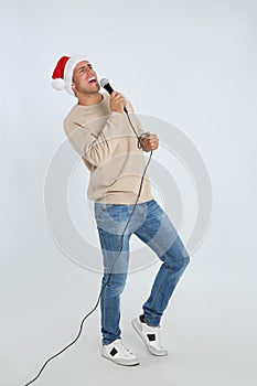 Emotional man in Santa Claus hat singing with microphone on white background. Christmas music