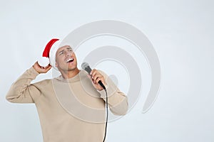 Emotional man in Santa Claus hat singing with microphone on white background, space for text. Christmas music