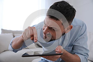 Emotional man with tablet at home. Online hate concept