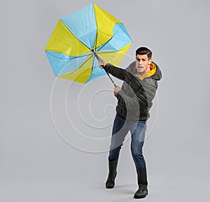 Emotional man with umbrella caught in gust of wind on grey background