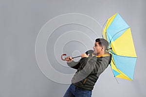 Emotional man with umbrella caught in gust of wind on grey background