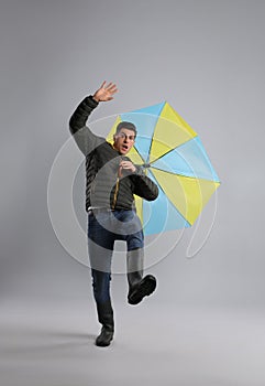 Emotional man with umbrella caught in gust of wind on grey background