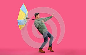 Emotional man with umbrella caught in gust of wind on pink background