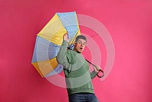 Emotional man with umbrella caught in gust of wind on pink background