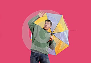 Emotional man with umbrella caught in gust of wind on pink background