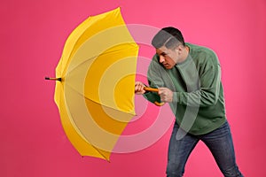 Emotional man with umbrella caught in gust of wind on pink background