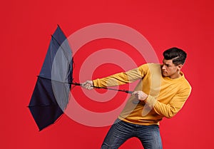 Emotional man with umbrella caught in gust of wind on red background