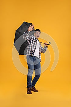 Emotional man with umbrella caught in gust of wind on yellow background