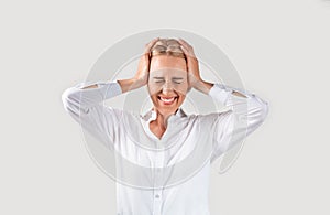 Emotional mature businesswoman holding her head in disbelief on light background