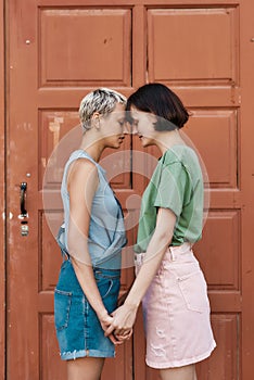 Emotional moment. Young female couple, two women touching foreheads, holding hands while standing in front of the door