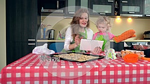 Emotional mother and daughter girl studying sweets recipes on tablet computer