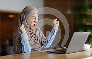 Emotional muslim woman in headscarf looking at laptop screen