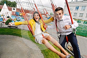 Emotional newlyweds screaming while riding on high carousel in amusement park. Expressive wedding couple at carnival.