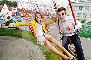 Emotional newlyweds screaming while riding on high carousel in amusement park. Expressive wedding couple at carnival.