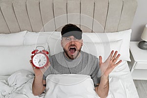Emotional overslept man with clock in bed, above view. Being late concept