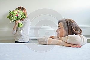 Emotional photo of mother and daughter, girl with bouquet of flowers covered her face