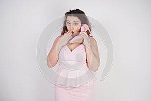 Emotional plump woman in pink dress talking and gossips on the Shoe like on the phone on a white Studio background