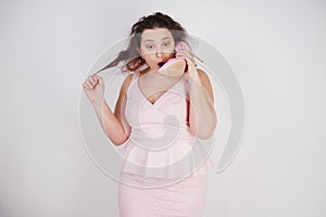 Emotional plump woman in pink dress talking and gossips on the Shoe like on the phone on a white Studio background