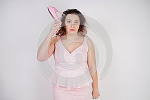 Emotional plump woman in pink dress talking and gossips on the Shoe like on the phone on a white Studio background