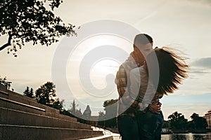 Emotional portrait of the beautiful loving couple hugging in the town street during the sunset. The girl is shaking her